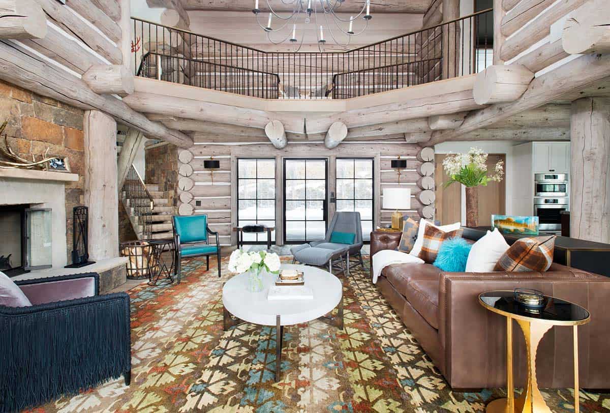 Two-story great room with log beams, loft railing, chandelier, and leather sofa on patterned rug