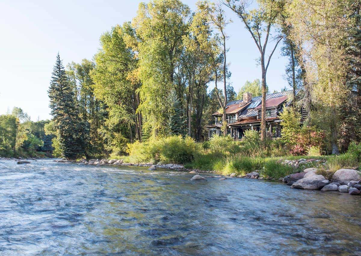 Log cabin viewed across a rushing river, framed by trees