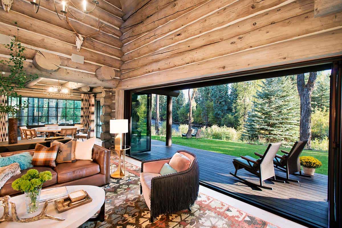 Living area with log walls opening onto a deck and forest view