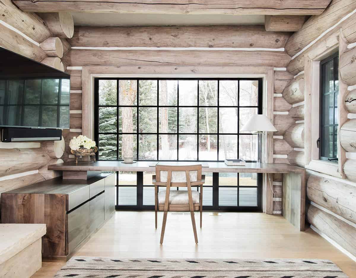Home office with built-in desk framed by a large log-cabin window