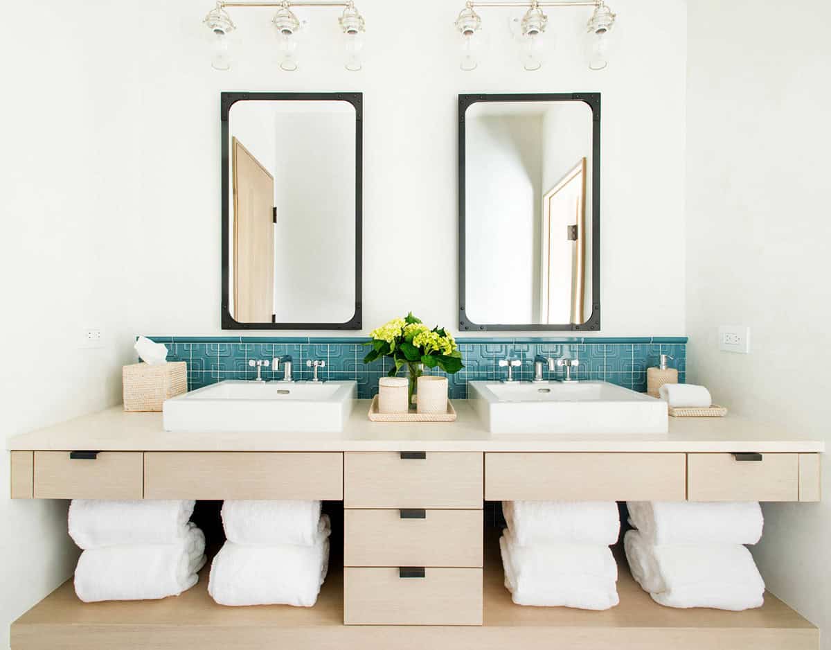 Bathroom double vanity with teal patterned tile backsplash and rolled towel storage