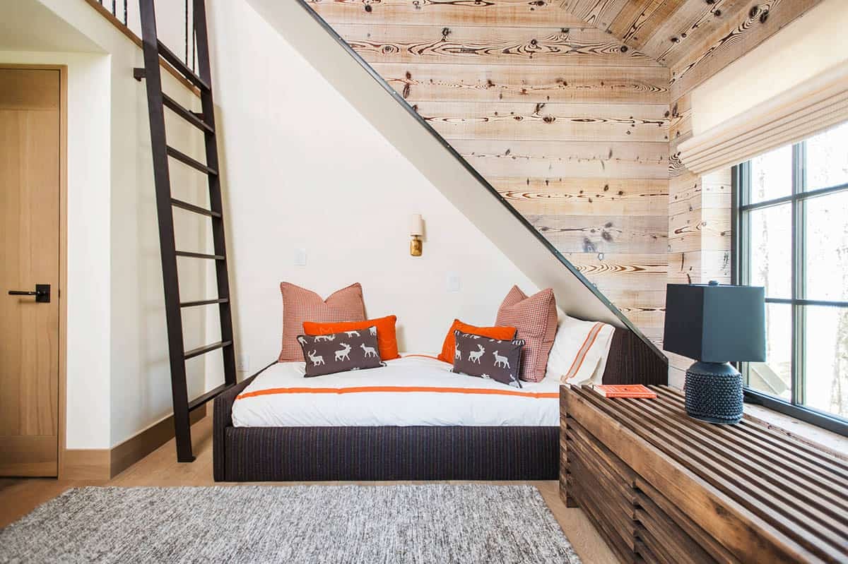 Guest bedroom tucked under a staircase with plank-wood walls and orange accent pillows