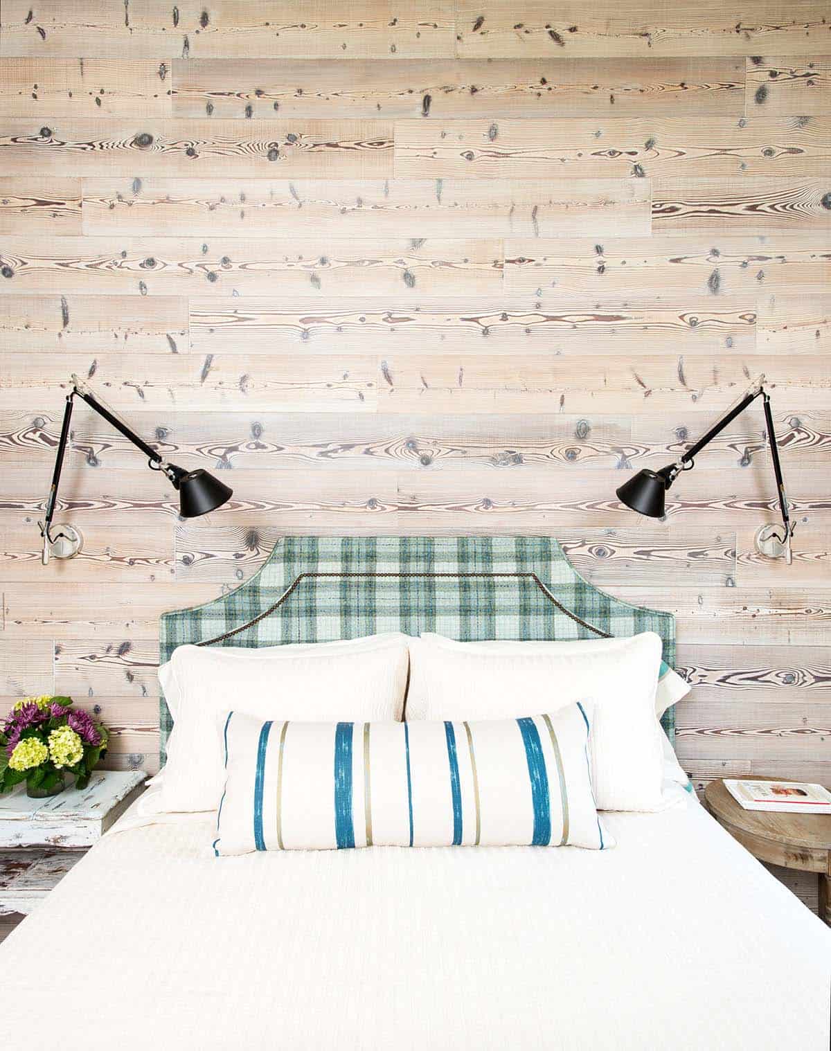 Bed with plaid headboard against a whitewashed wood-plank wall, flanked by swing-arm lamps