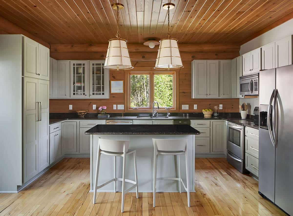 Log cabin kitchen with sage green cabinets, dark granite counters, and pendant lights over an island