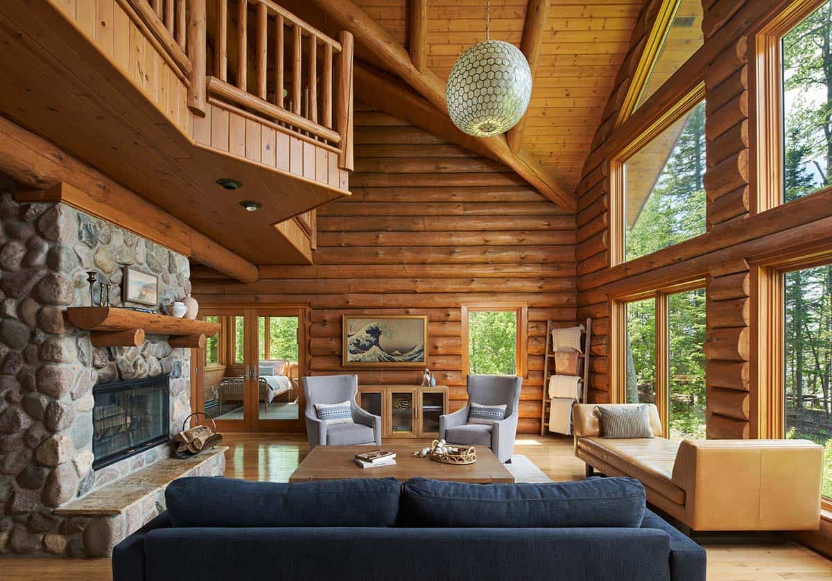 Great room with stone fireplace, loft railing, navy sofa, and lake-view windows