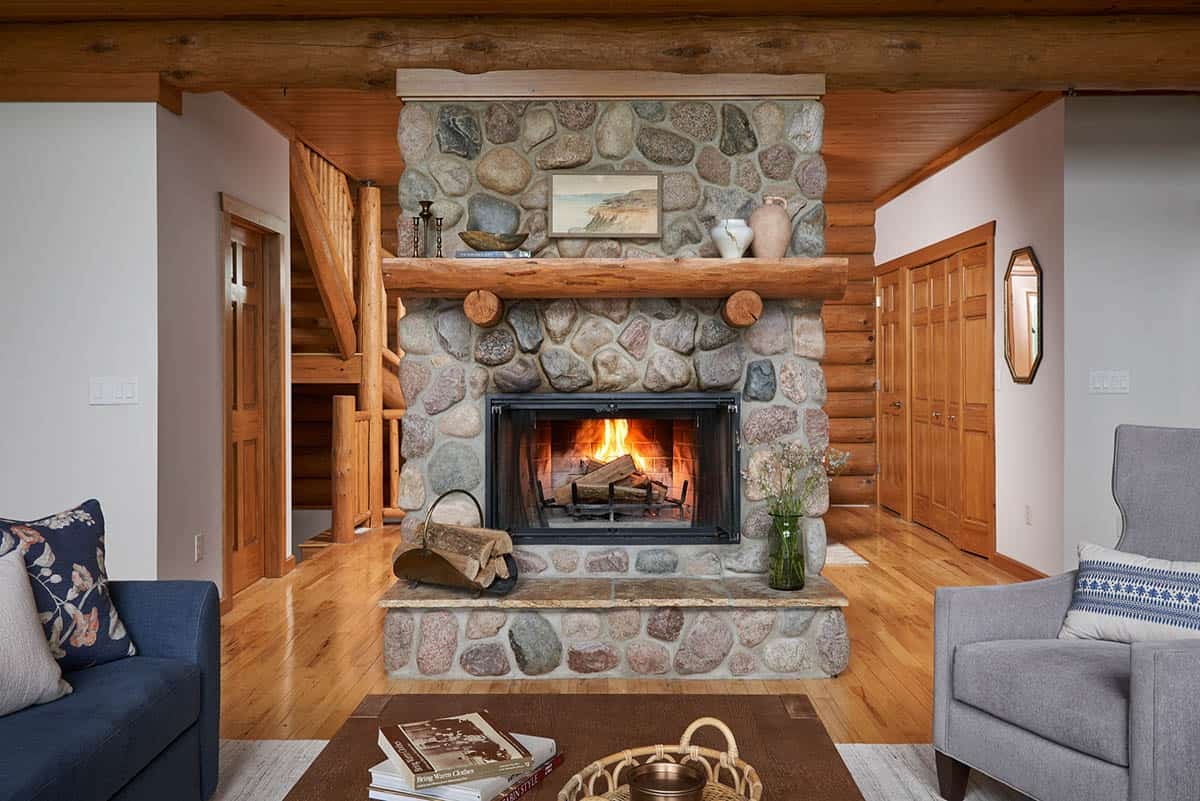 Close-up of river-stone fireplace with wood mantel and lit fire