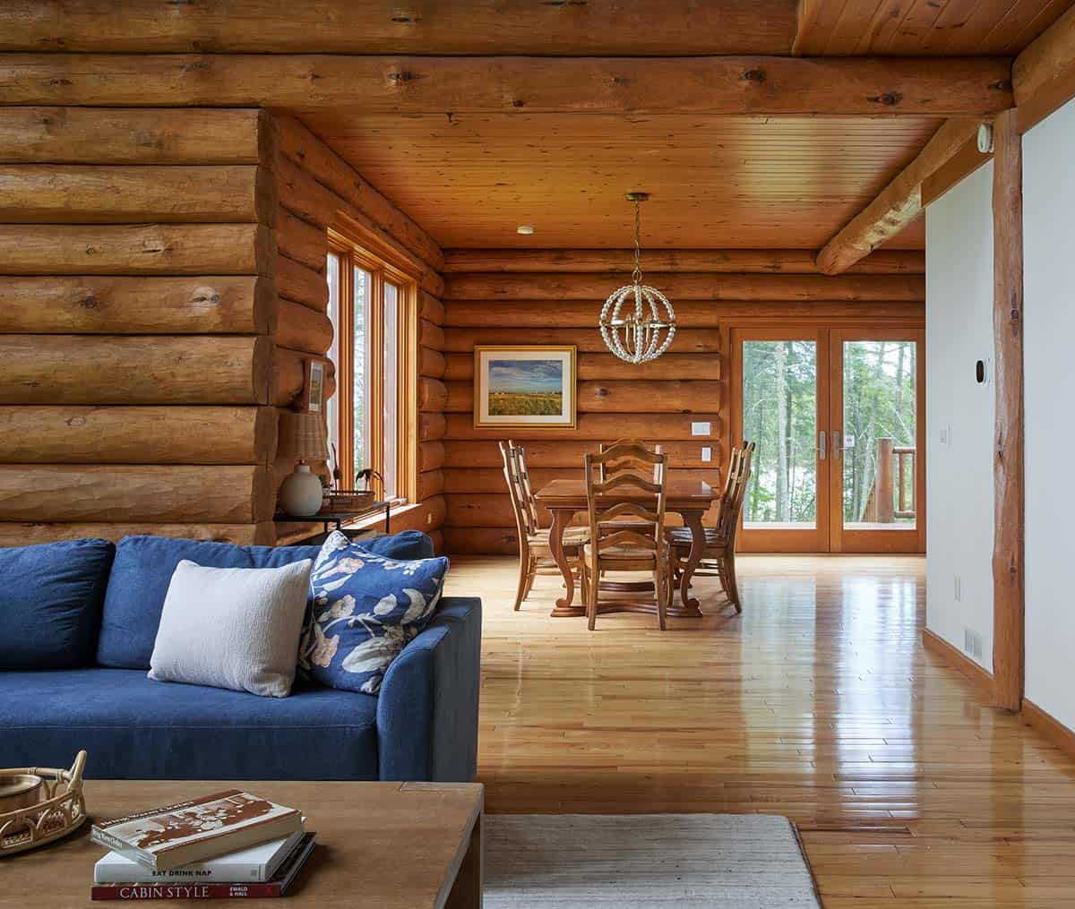 Open living and dining area with log walls, navy sofa, and wood dining table