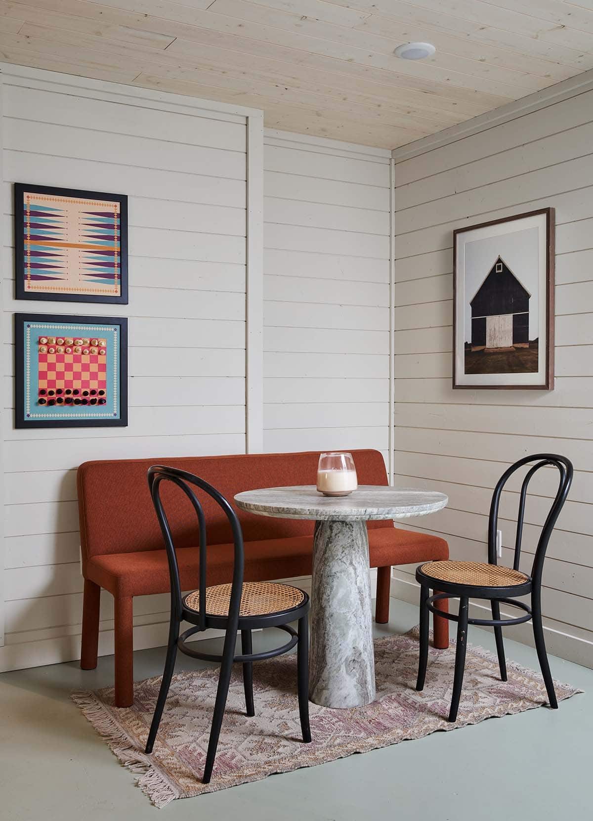 Small breakfast nook with rust-colored bench, marble table, and framed game boards