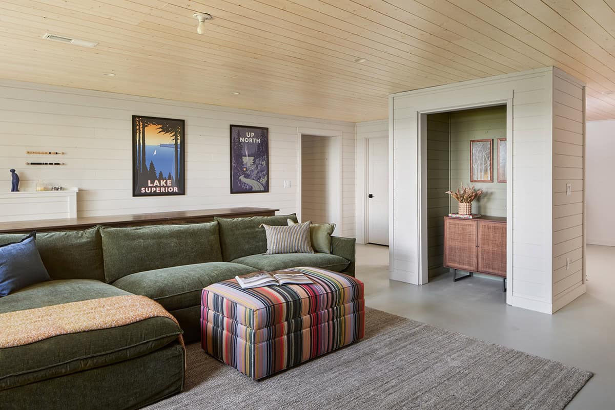 Basement family room with green sectional, striped ottoman, and travel posters