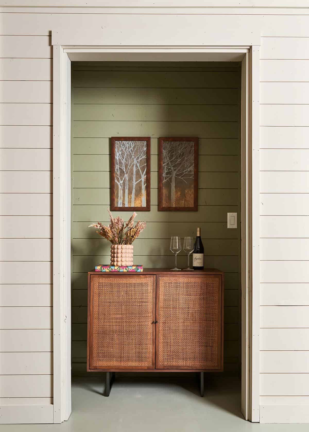 Alcove nook with sage green walls, rattan cabinet, and tree artwork
