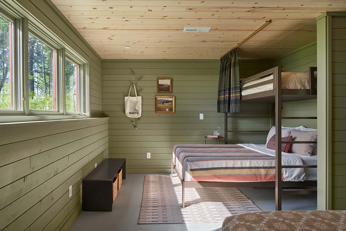 Green-paneled bunk room with striped bedding and windows