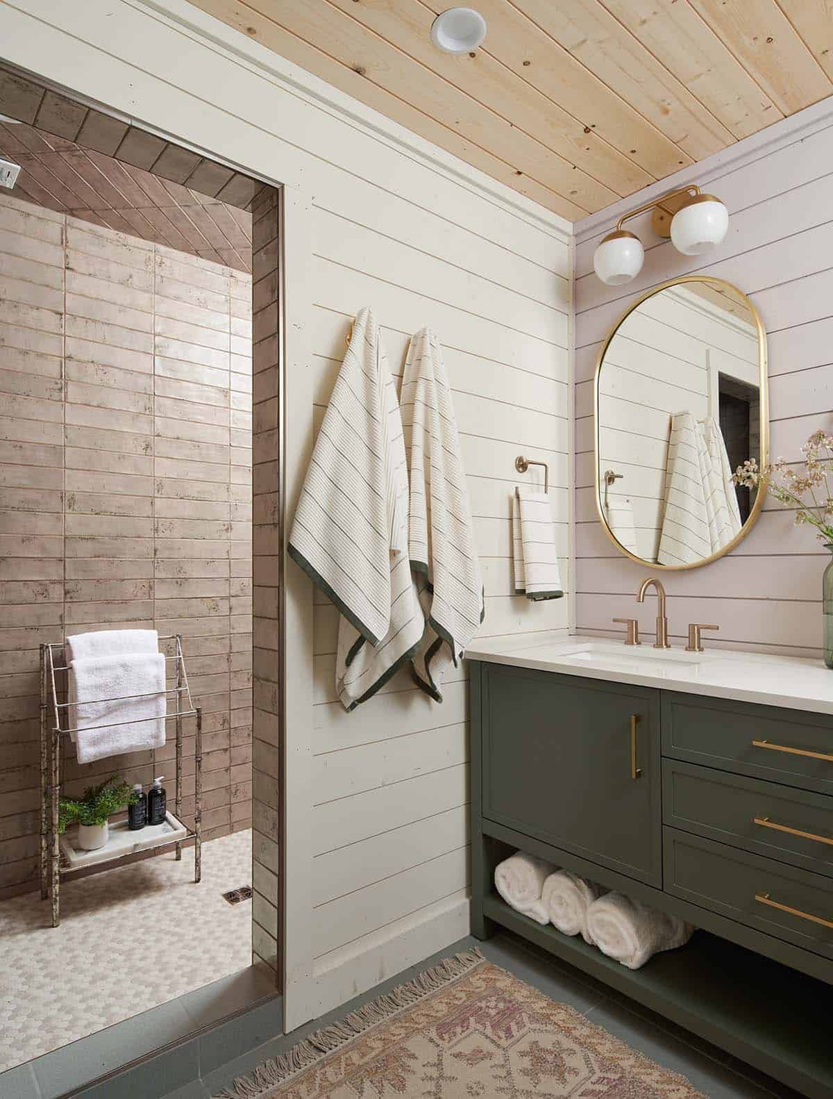 Bathroom with green vanity, brass fixtures, oval mirror, and tiled shower