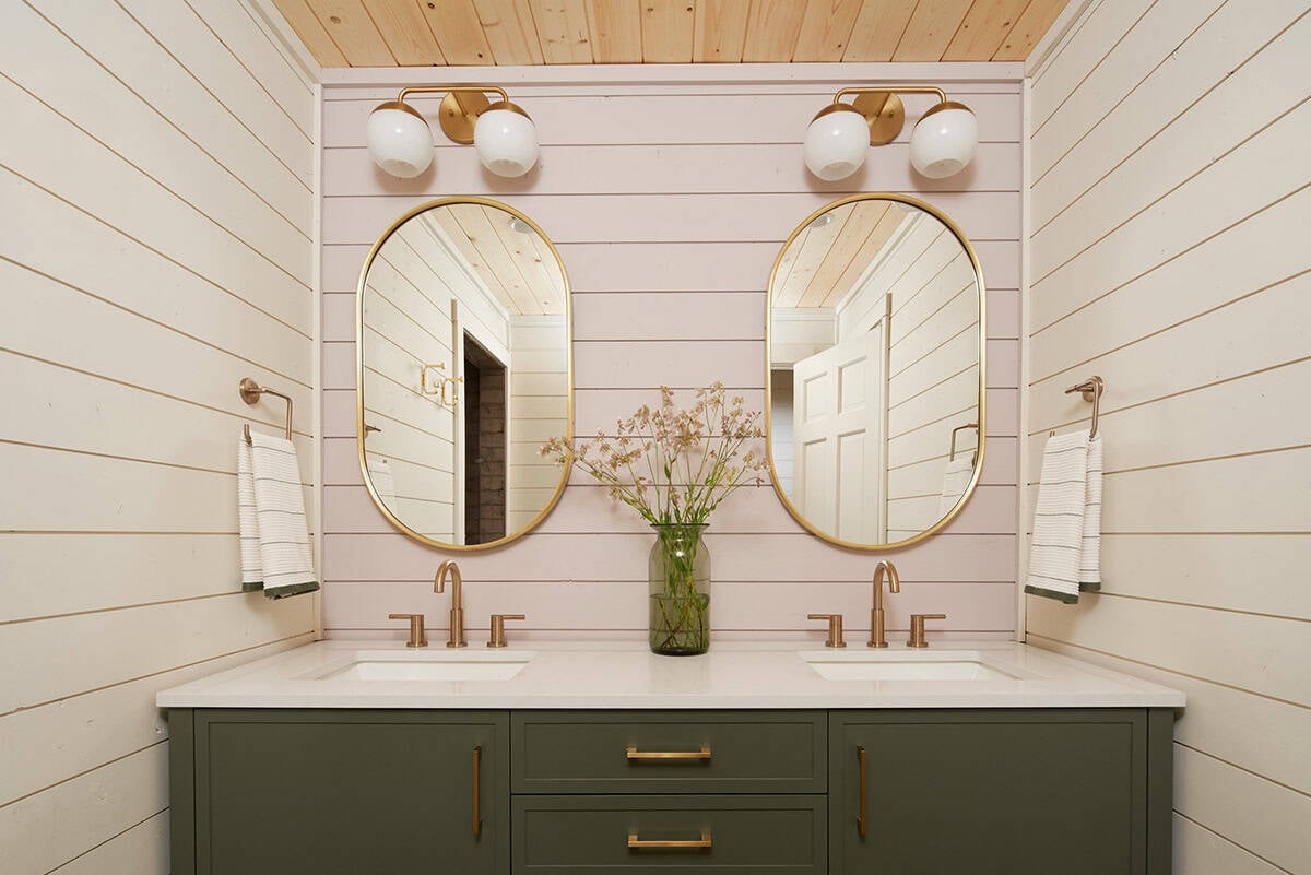 Double vanity bathroom with brass mirrors, green cabinetry, and pink walls