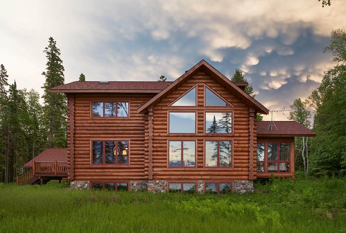 Two-story log cabin exterior with large gabled window wall under a dramatic sky