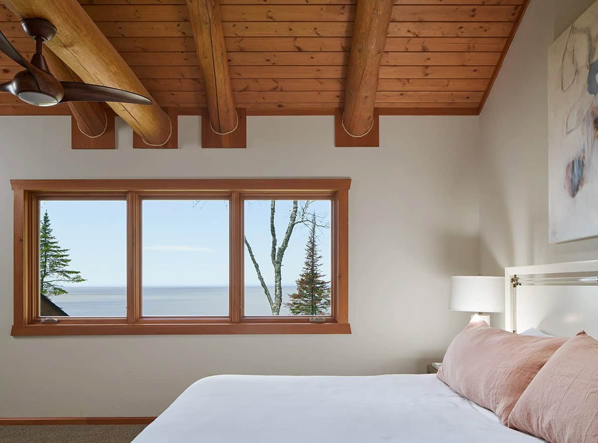 Bedroom with exposed log beams and window framing a Lake Superior view