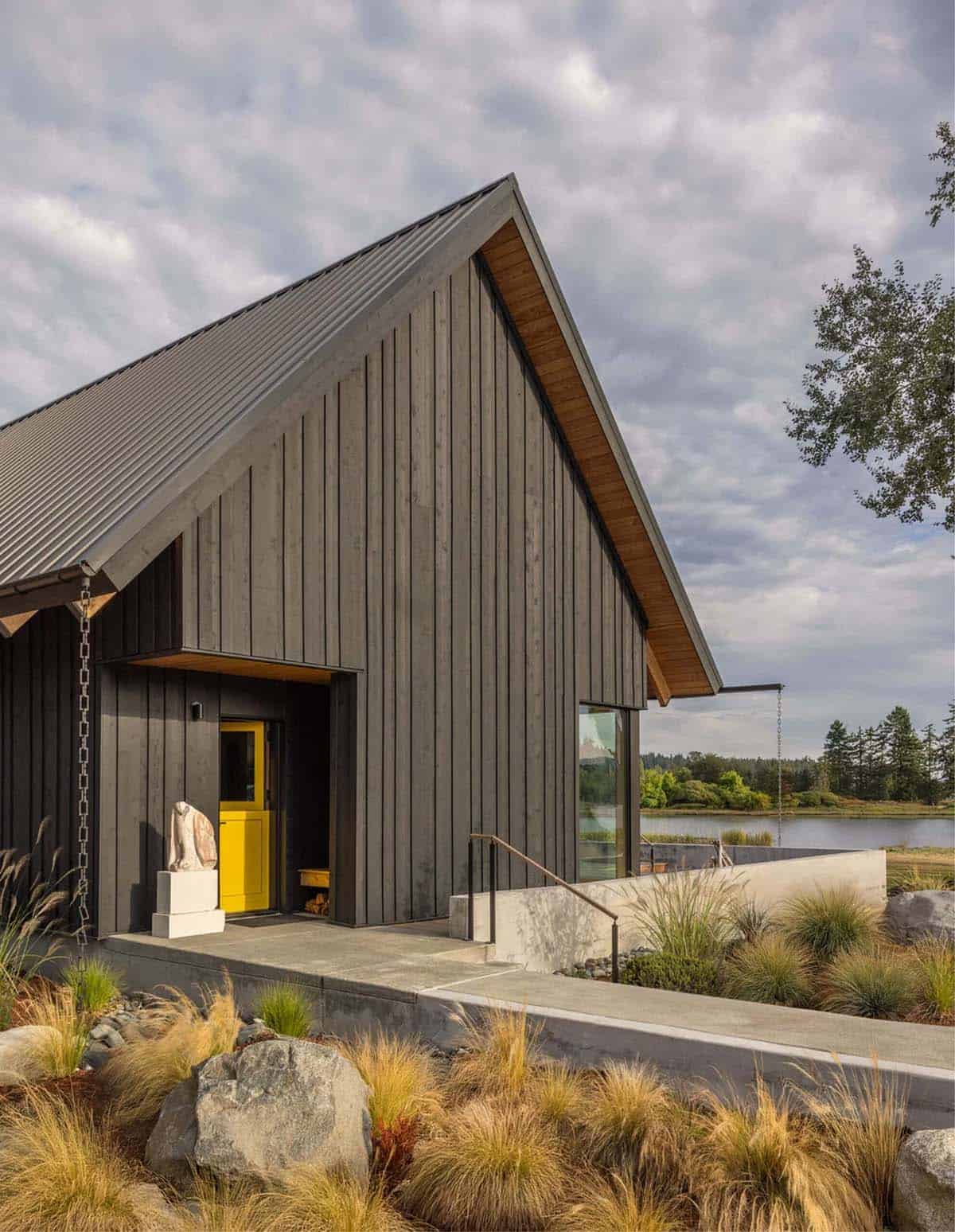 Angled view of black board-formed exterior with yellow front door and water view