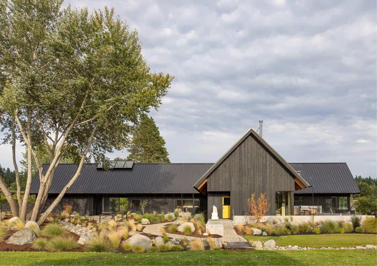 Front elevation of black farmhouse-style home with courtyard landscaping and yellow door