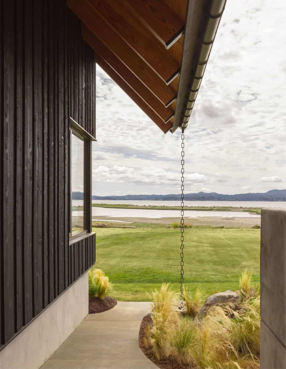Rain chain hanging from wood eave overlooking lawn and inlet waterfront