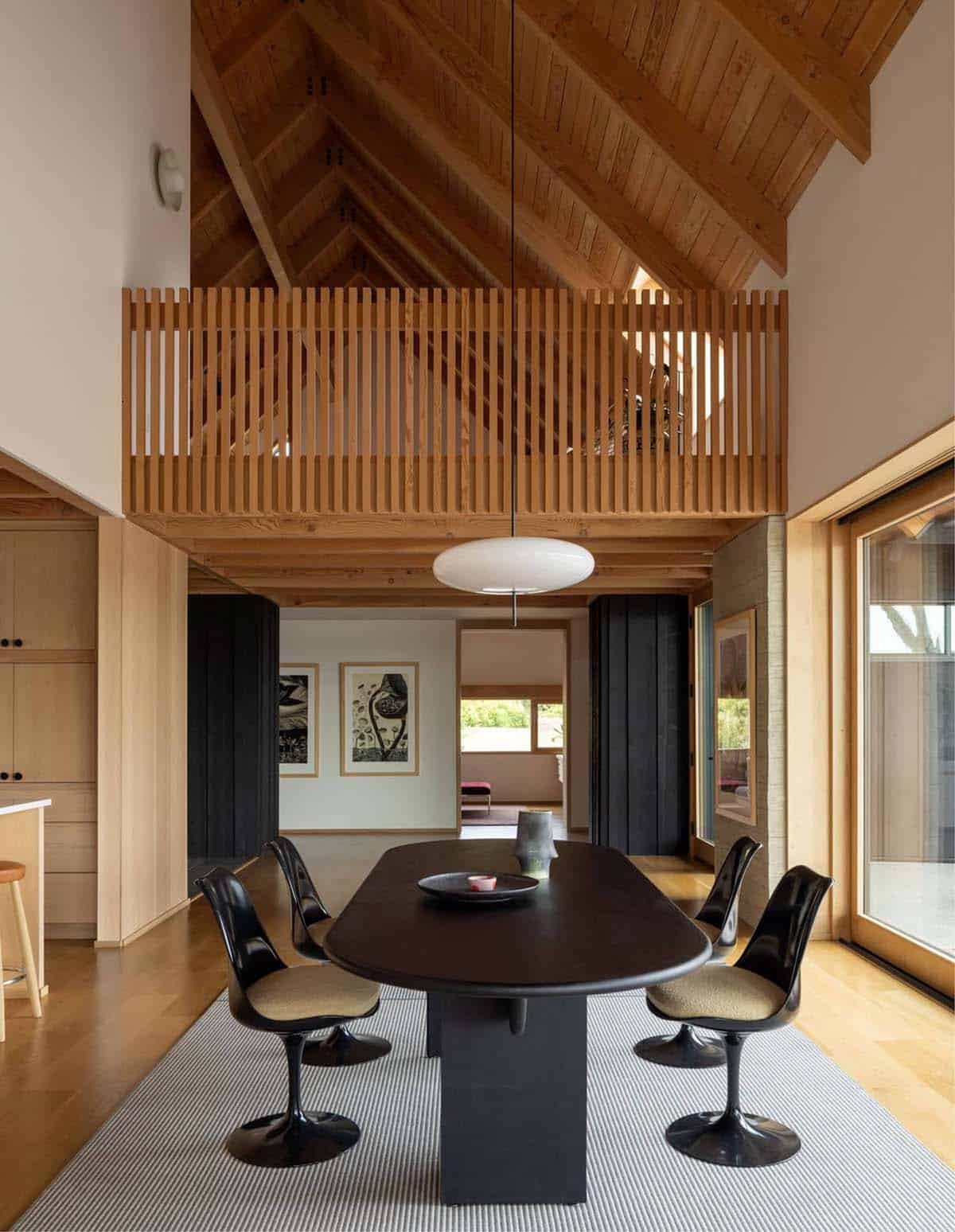 Dining room with black oval table beneath open wood-slat loft railing