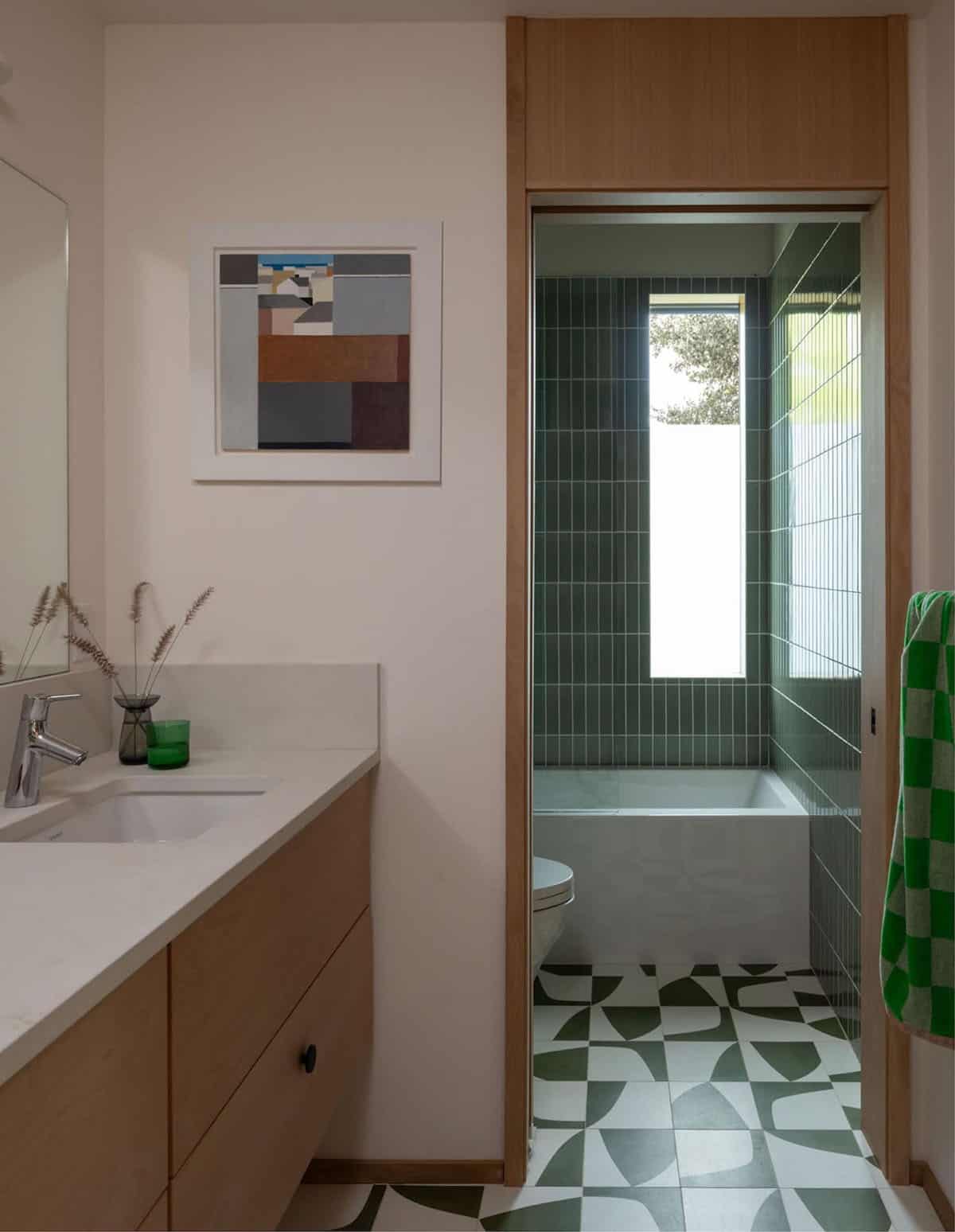 Bathroom vanity with view into green-tiled tub and patterned floor