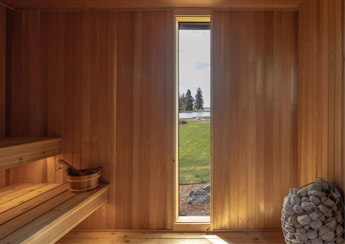Cedar-lined sauna interior with tall window overlooking lawn and water