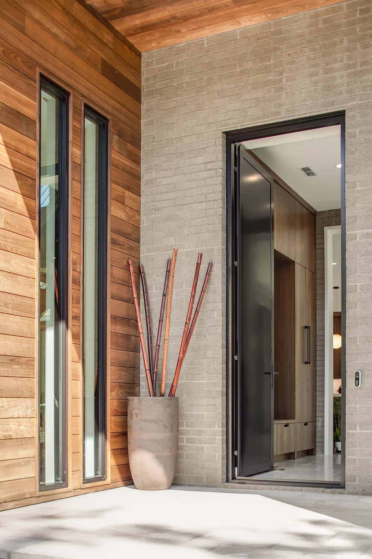 Front entry with black pivot door, cedar paneling, and brick facade