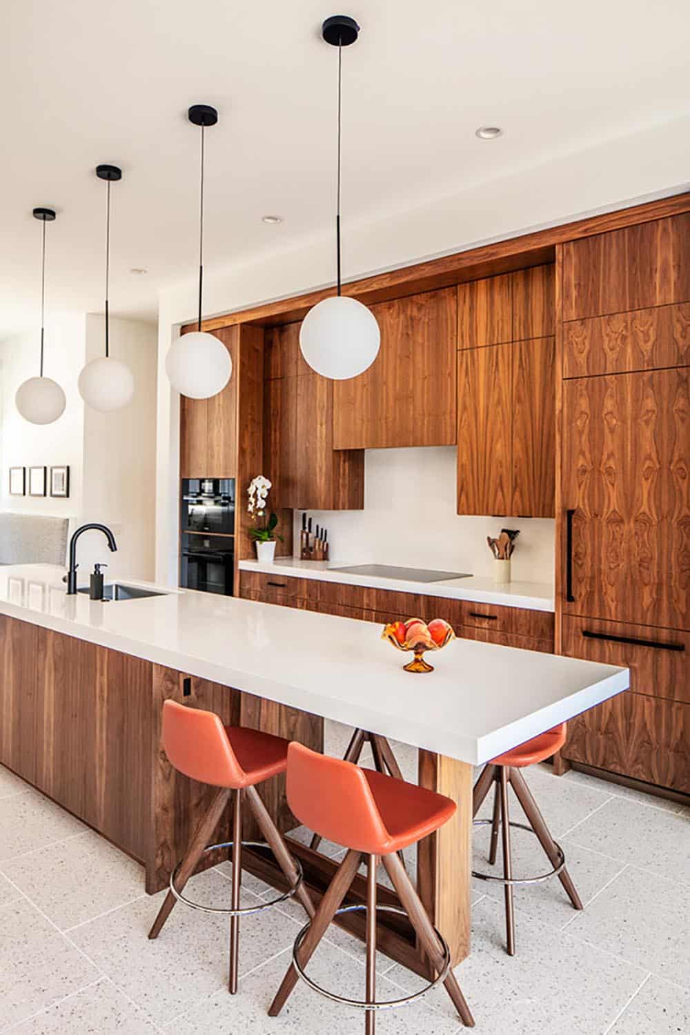 Modern kitchen with walnut cabinetry, white island, globe pendant lights, and orange bar stools