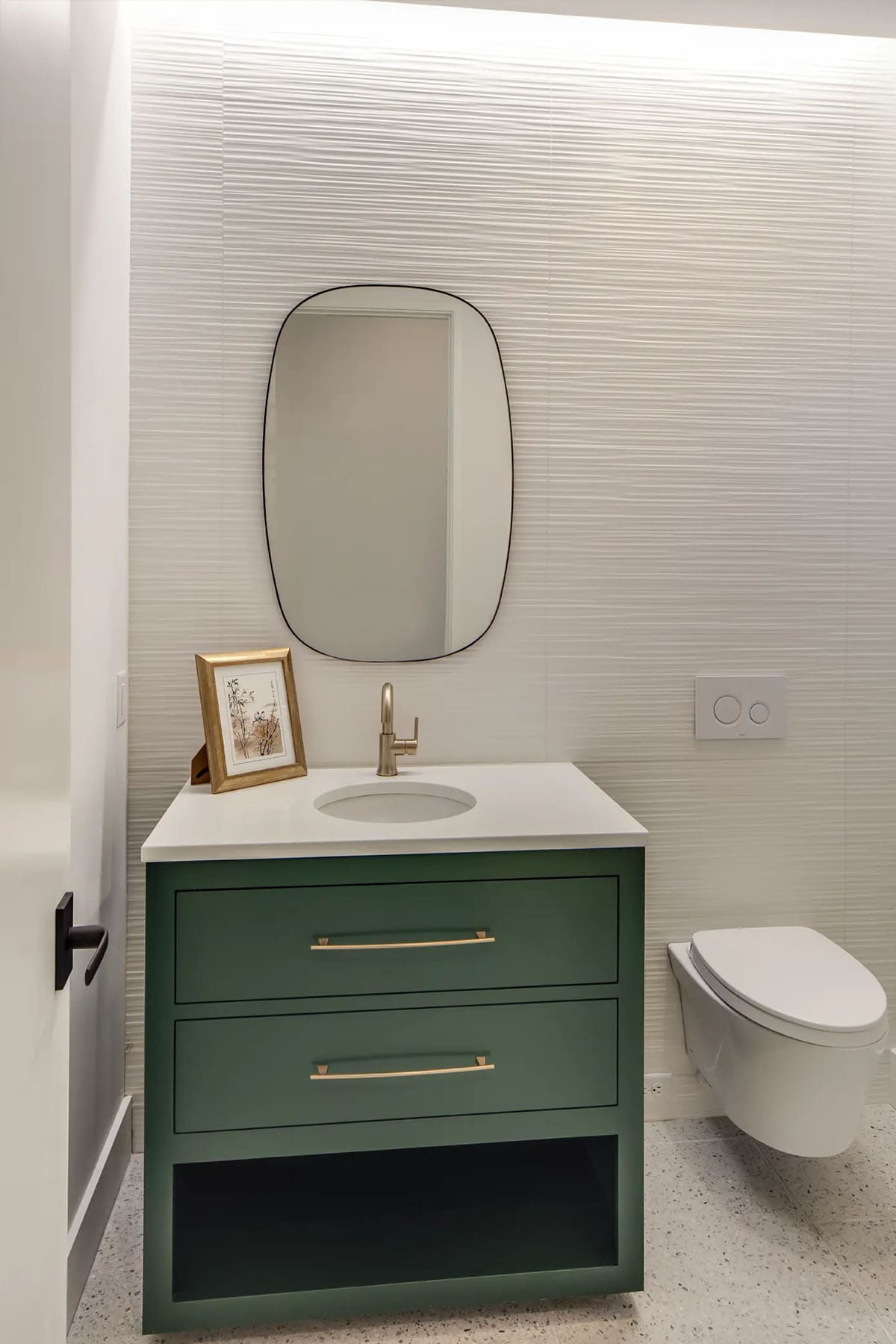 Powder room with green vanity, oval mirror, and textured wallpaper