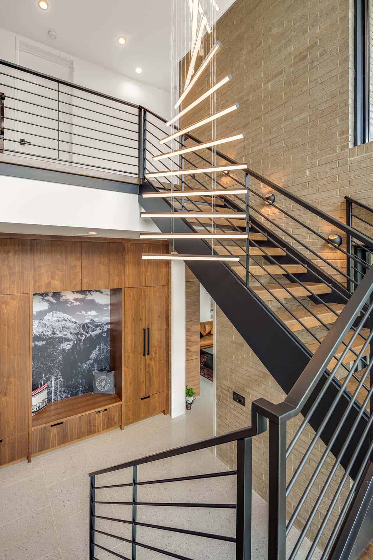 Interior stairwell with wood treads, black metal railing, and linear pendant light fixture