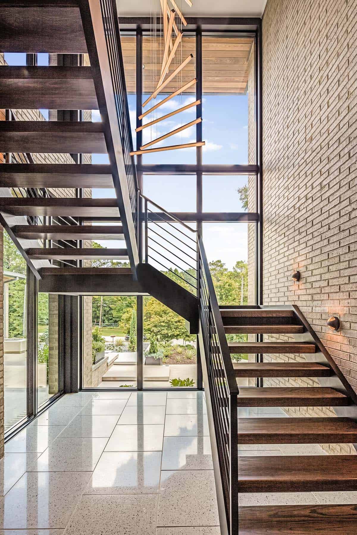 Floating staircase against brick wall with tall glass window and geometric pendant light