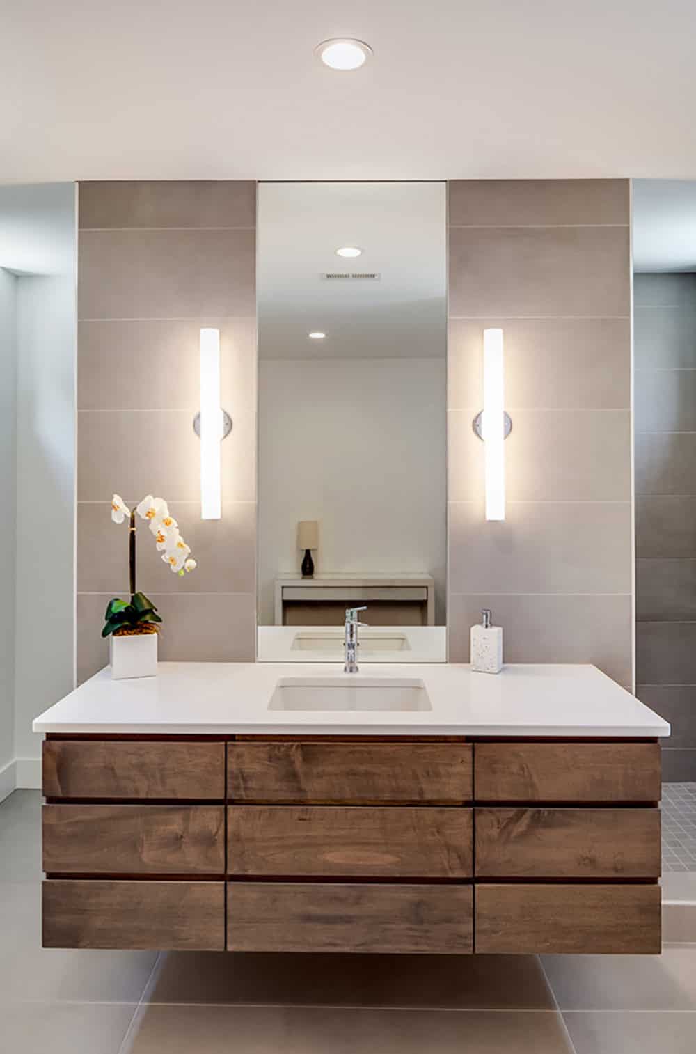 Bathroom vanity with wood cabinetry, tile accent wall, and vertical sconce lighting