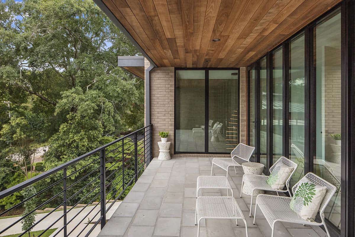 Covered balcony with wood ceiling, wicker lounge chairs, and tree canopy view