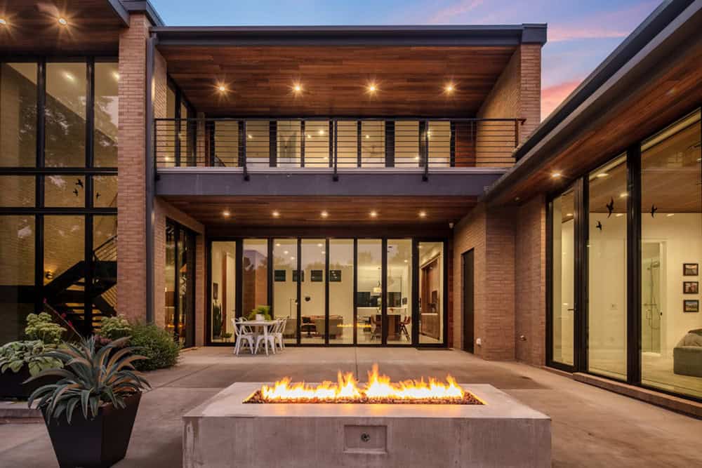 Twilight courtyard with linear gas fire pit and glowing glass-walled interiors