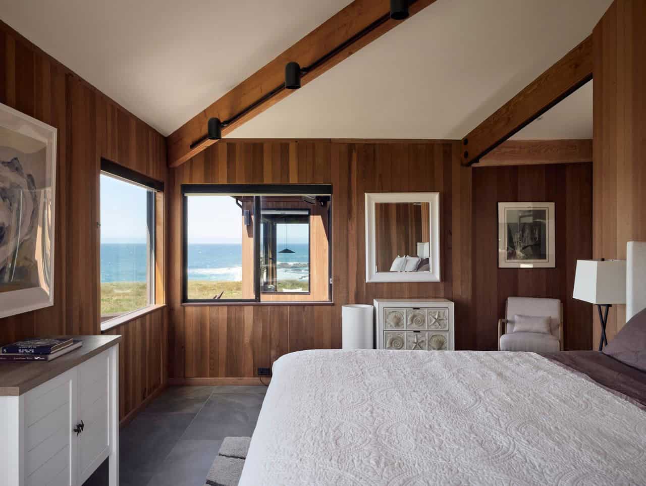 Primary bedroom with ocean-view window and wood-paneled walls
