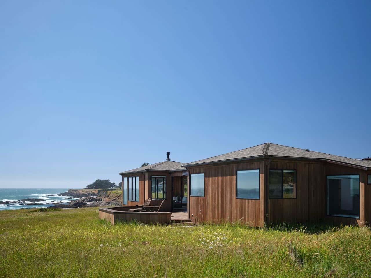Wide exterior view of bluff home with wraparound deck and ocean backdrop