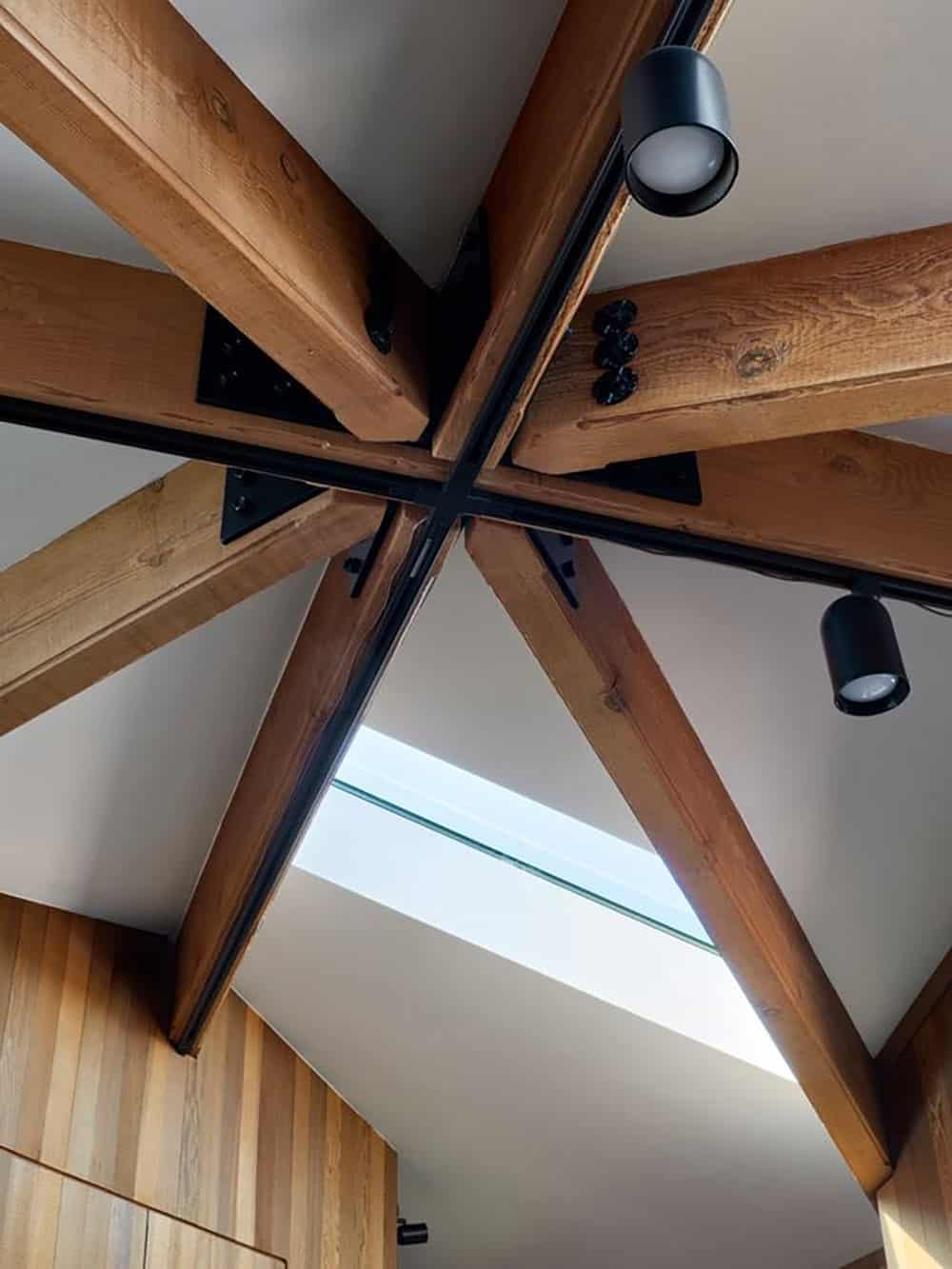 Close-up of intersecting wood roof beams with steel connector and skylight