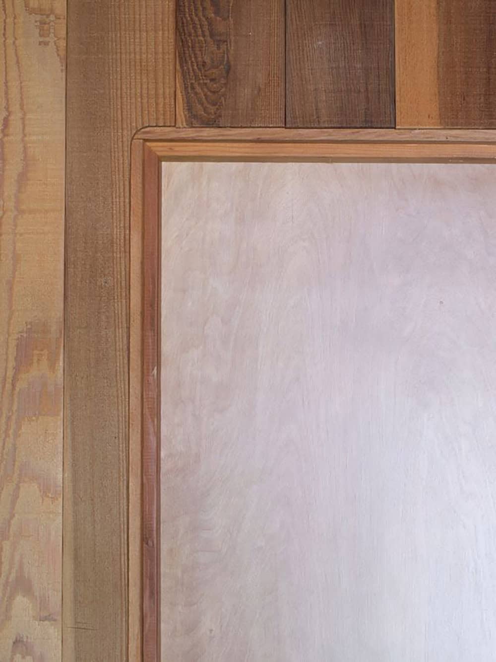 Corner detail of cedar-framed door trim against paneled wall