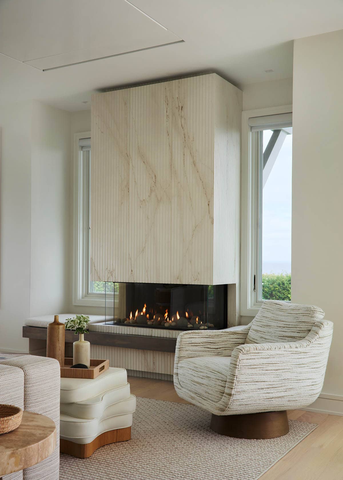 Stone-clad three-sided fireplace with cream swivel chair
