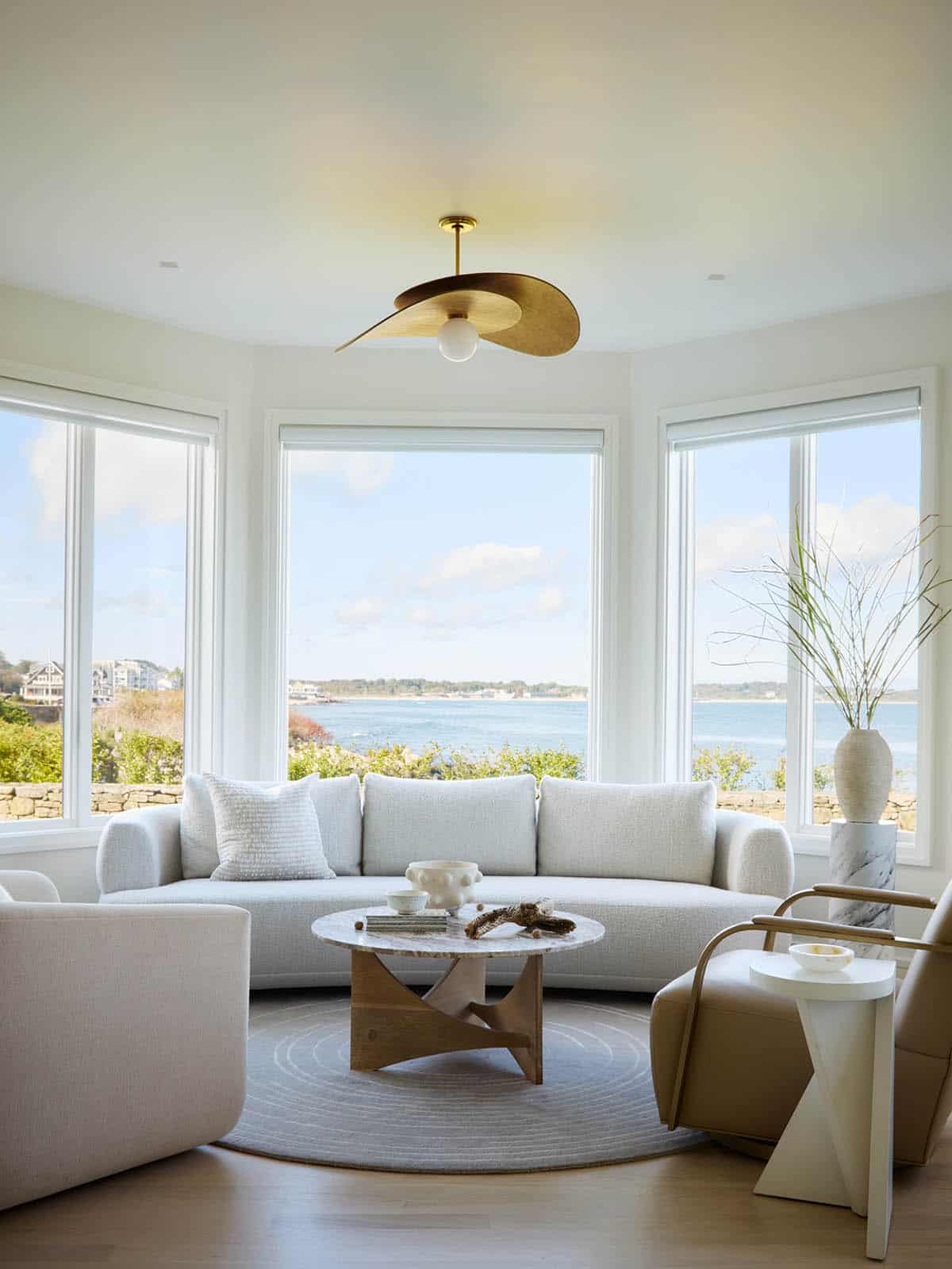 Curved sofa seating area with brass ceiling fan and ocean view