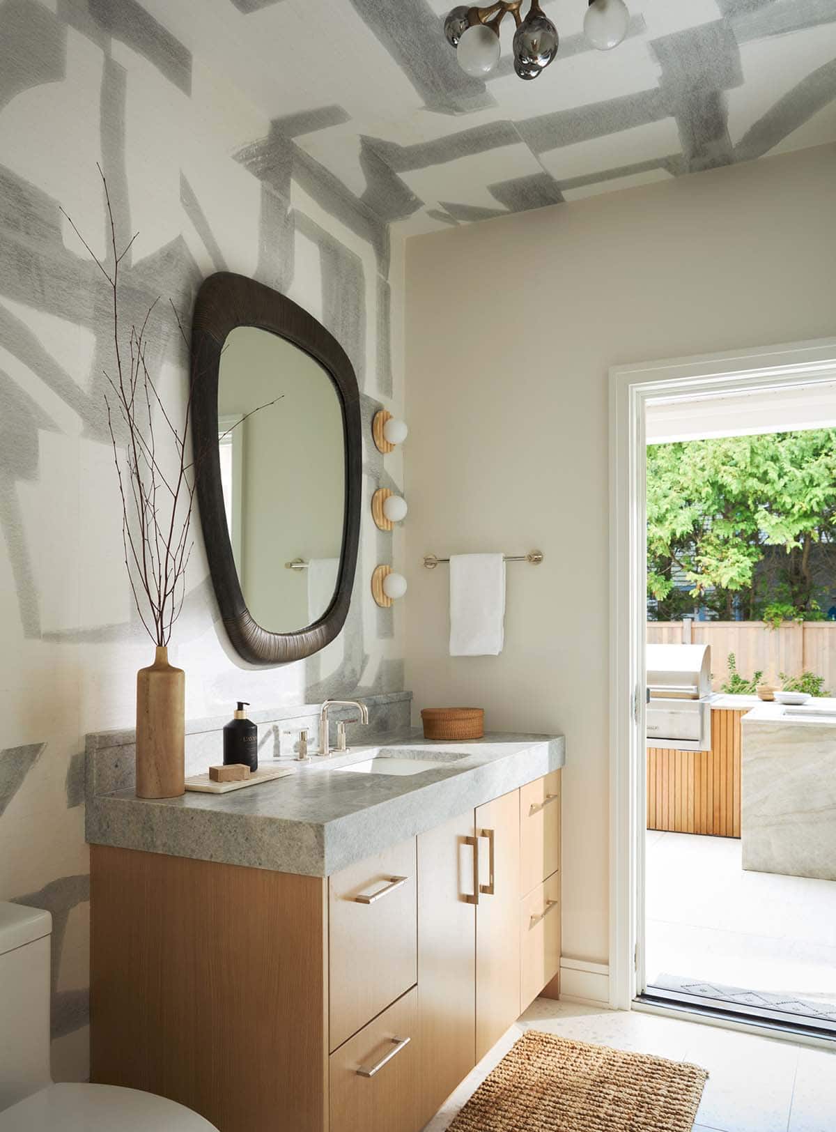 Powder room vanity with sculptural mirror and outdoor kitchen view