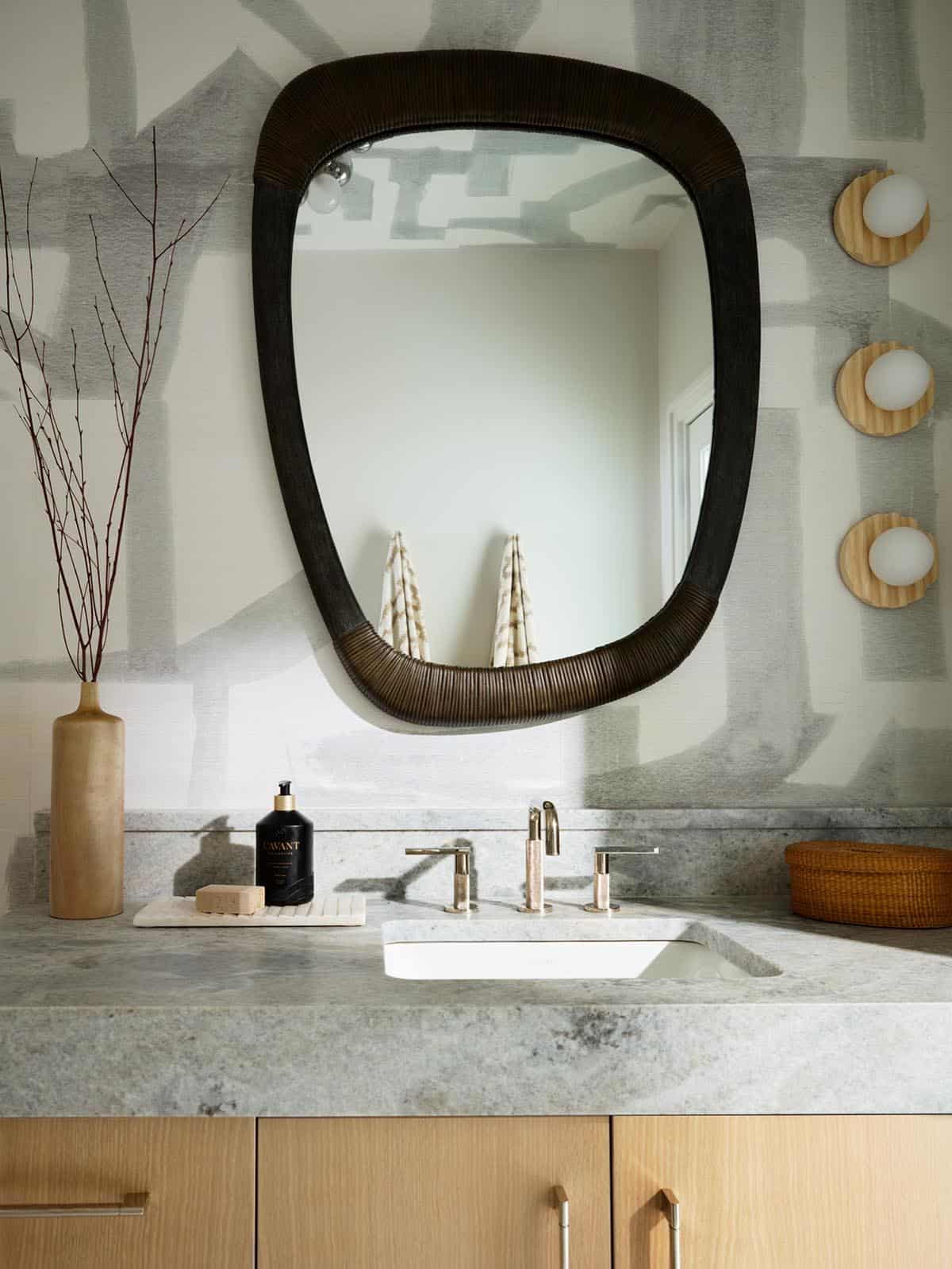 Sculptural black mirror above stone bathroom vanity