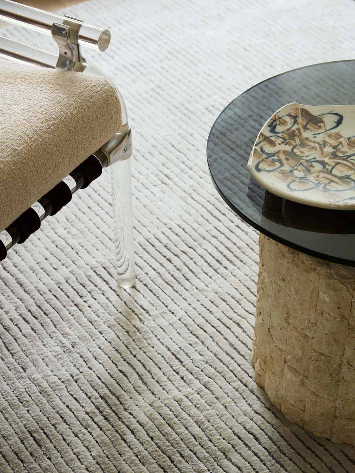 Lucite chair leg and stone side table detail on textured rug