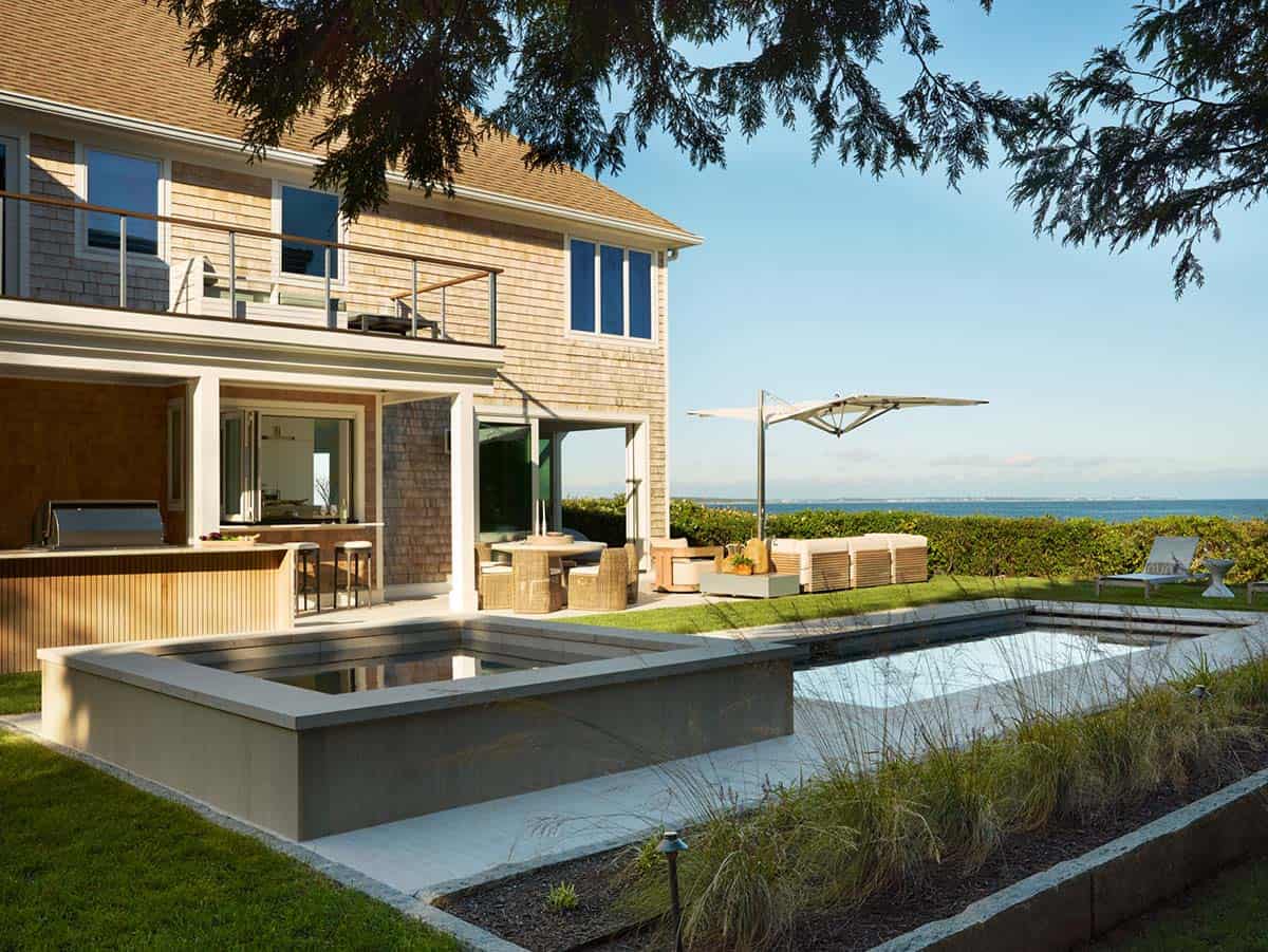 Rear exterior of shingled home with pool and ocean view at sunset