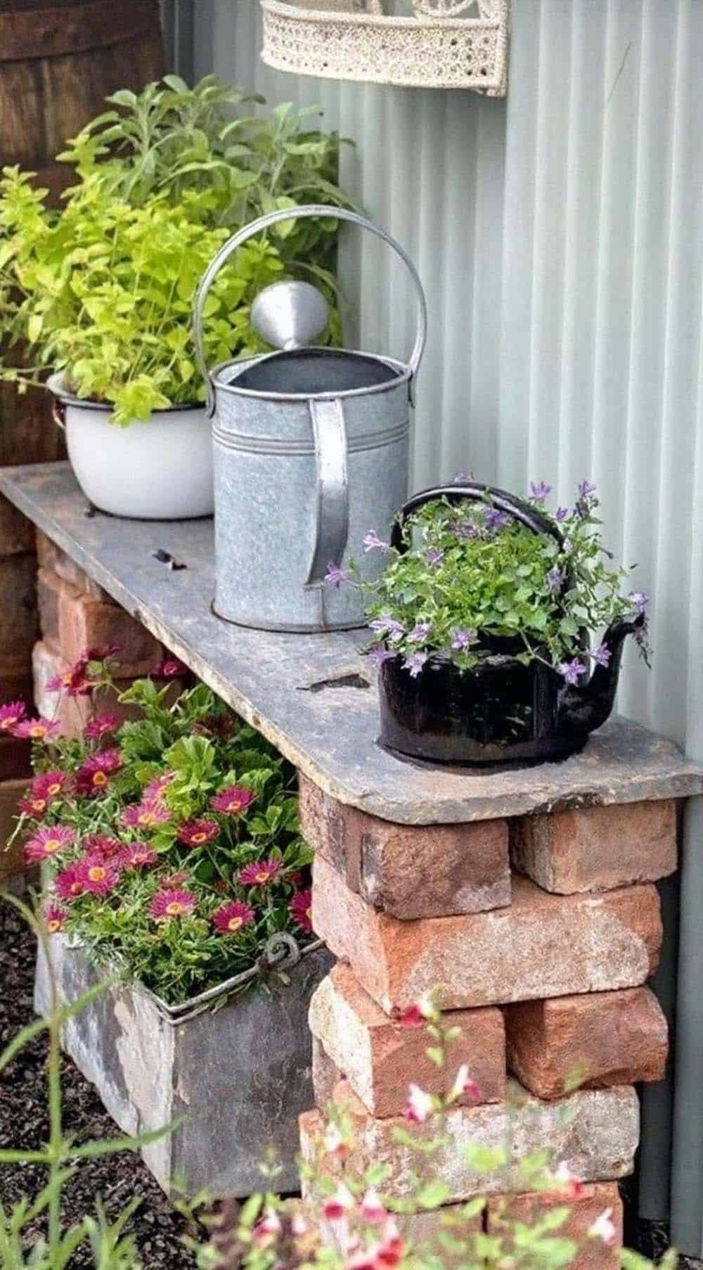Stacked bricks supporting a slate bench used as a plant stand for potted herbs and a repurposed kettle planter