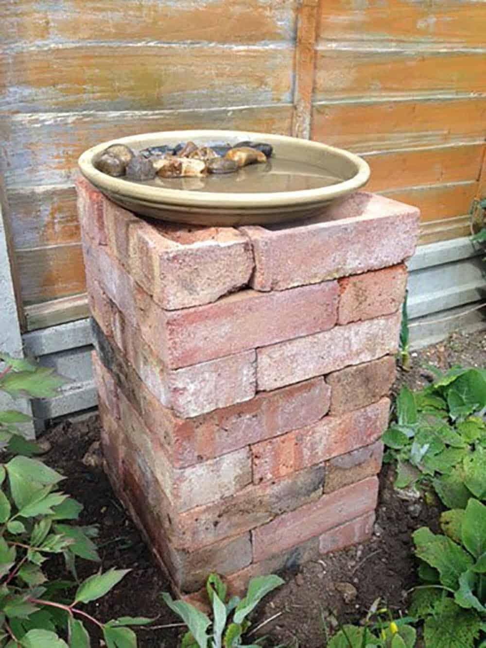 Reclaimed bricks stacked into a pedestal topped with a ceramic dish birdbath filled with water and stones