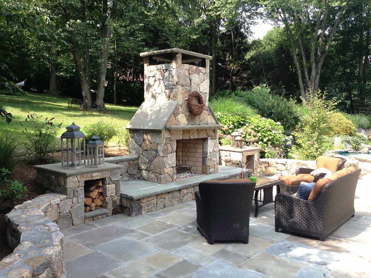Stone fireplace with built-in log holders on a bluestone patio