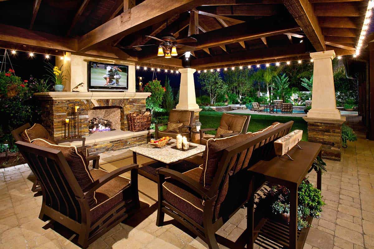 Stacked stone fireplace with mounted TV on a covered patio at night