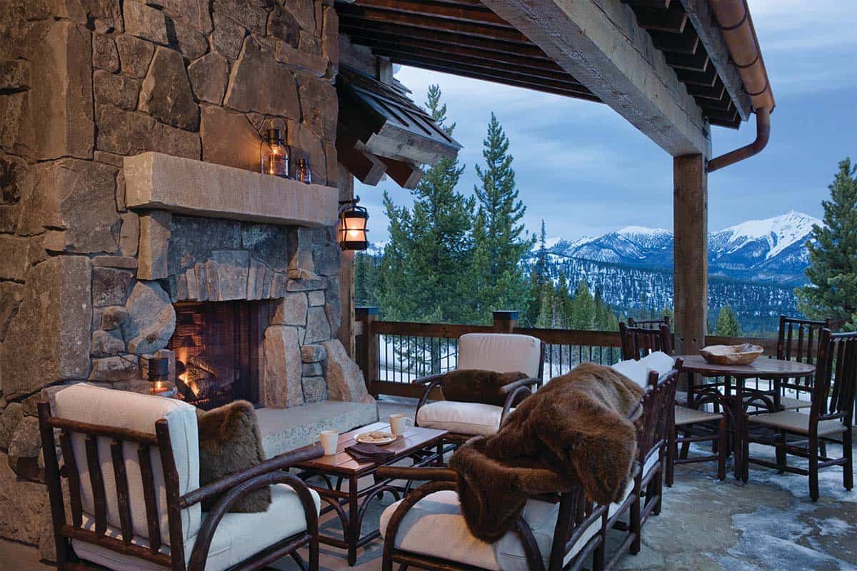 Rustic stone fireplace on a mountain-view deck with fur throws and seating