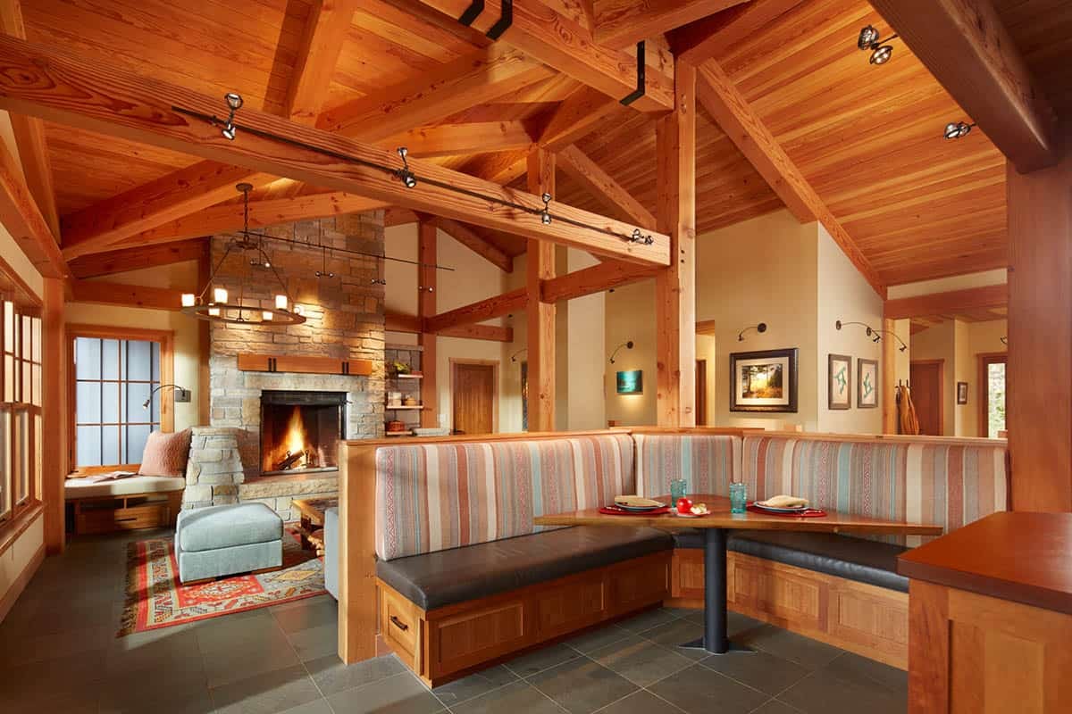 Built-in breakfast banquette beside stone fireplace under timber ceiling