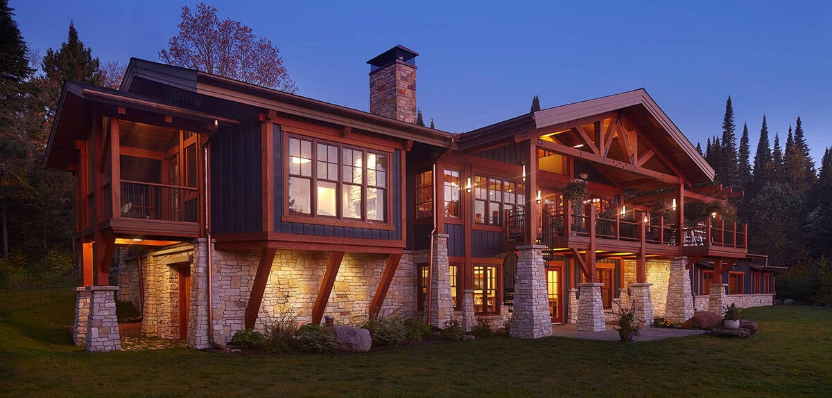 Twilight view of timber-frame lake house with lit windows and stone base